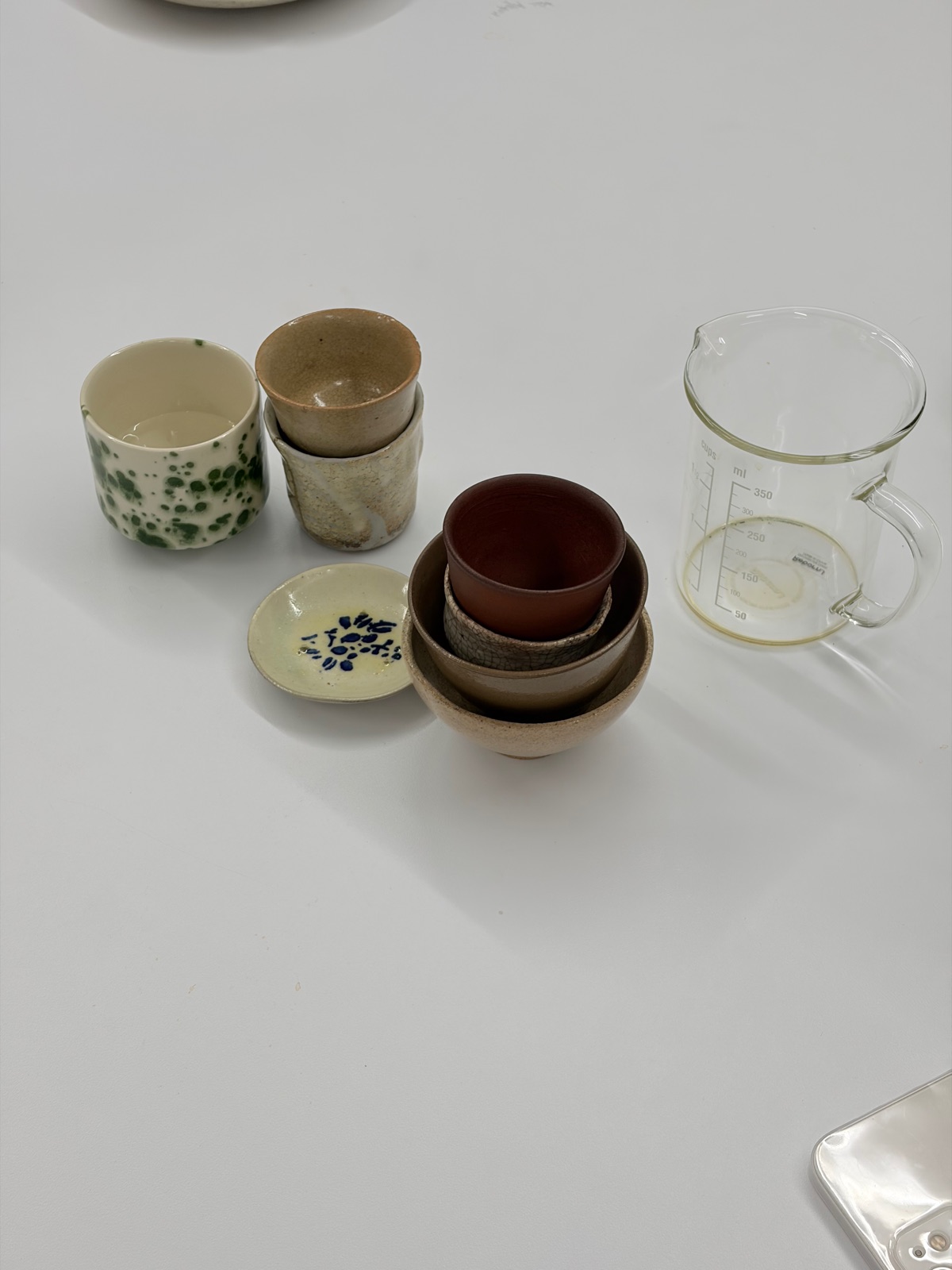 A table set with a glass measuring cup and handmade ceramic cups and plates in a variety of glazes 유리 계량컵과 다양한 유약의 수제 도자기 잔·접시들이 놓인 테이블