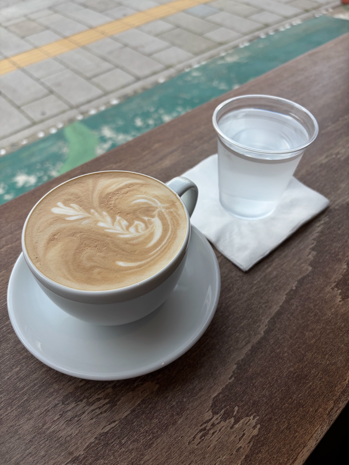 A warm Cafe Latte with latte art and a glass of water sit on an wooden table. 라떼아트가 그려진 따뜻한 카페라떼와 물 한 잔이 나무 테이블 위에 놓여 있다.
