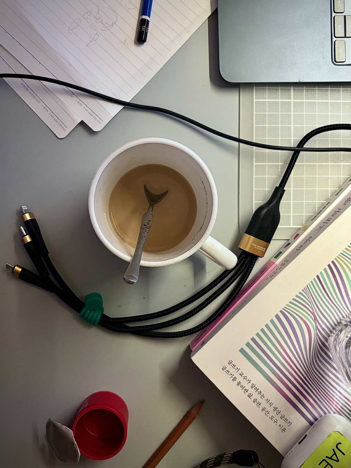 A desk workspace with a laptop, books, writing tools, and cables, alongside a cup of coffee 노트북, 책, 필기구, 케이블 등이 놓인 책상 위 작업 공간과 커피 한 잔